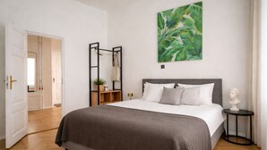 A bedroom with a bed, a nightstand, a bust on the nightstand, a painting on the wall, and a door leading to another room. - Nexus Rentals Tallinn (Tallinn)