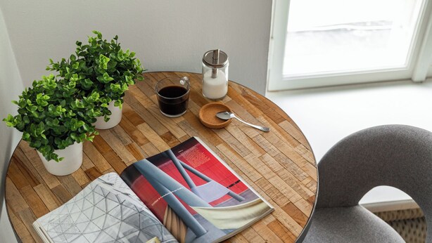A round wooden table with a magazine, a cup of coffee, a jar of sugar, and a plant. - Nexus Rentals Tallinn (Tallinn)