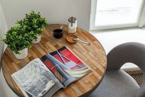 Una mesa redonda de madera con una revista, una taza de café, un frasco de azúcar y una planta.