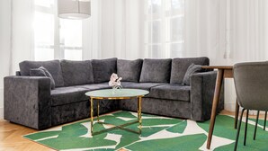 A modern living room with a grey sectional sofa, a small round table with a green rug, and a grey armchair. - Nexus Rentals Tallinn (Tallinn)