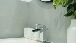A modern bathroom with a white sink, a mirror, and a potted plant.