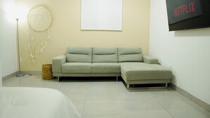 A modern living room with a sofa, a dreamcatcher, a flat-screen TV, and a wall-mounted artwork.