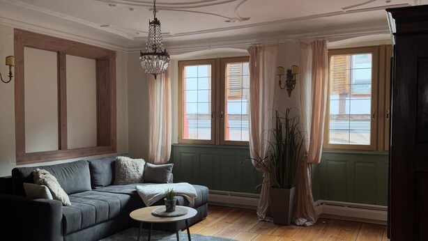 Un salon avec un canapé foncé, une table basse ronde et un lustre.