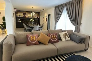 Un salon avec un canapé, des coussins, un tapis à rayures et, au fond, un coin repas.