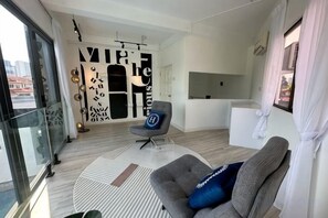 Una sala de estar moderna con un sofá, una silla, un tapete estampado y un ventanal que da a un balcón.