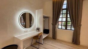 Habitació amb escriptori blanc, mirall rodó amb llums, cadira, finestra amb cortines i armari.