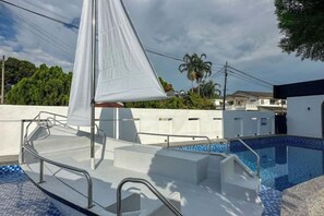 Una piscina con una cobertura de vela blanca, escalones de acceso y una zona de terraza con baldosas.