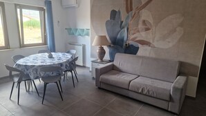 A dining area with a round table, chairs, a sofa, and a wall with a large floral mural.