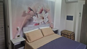 A bedroom with a bed, nightstands, a wall-mounted air conditioner, and a small table with a box.