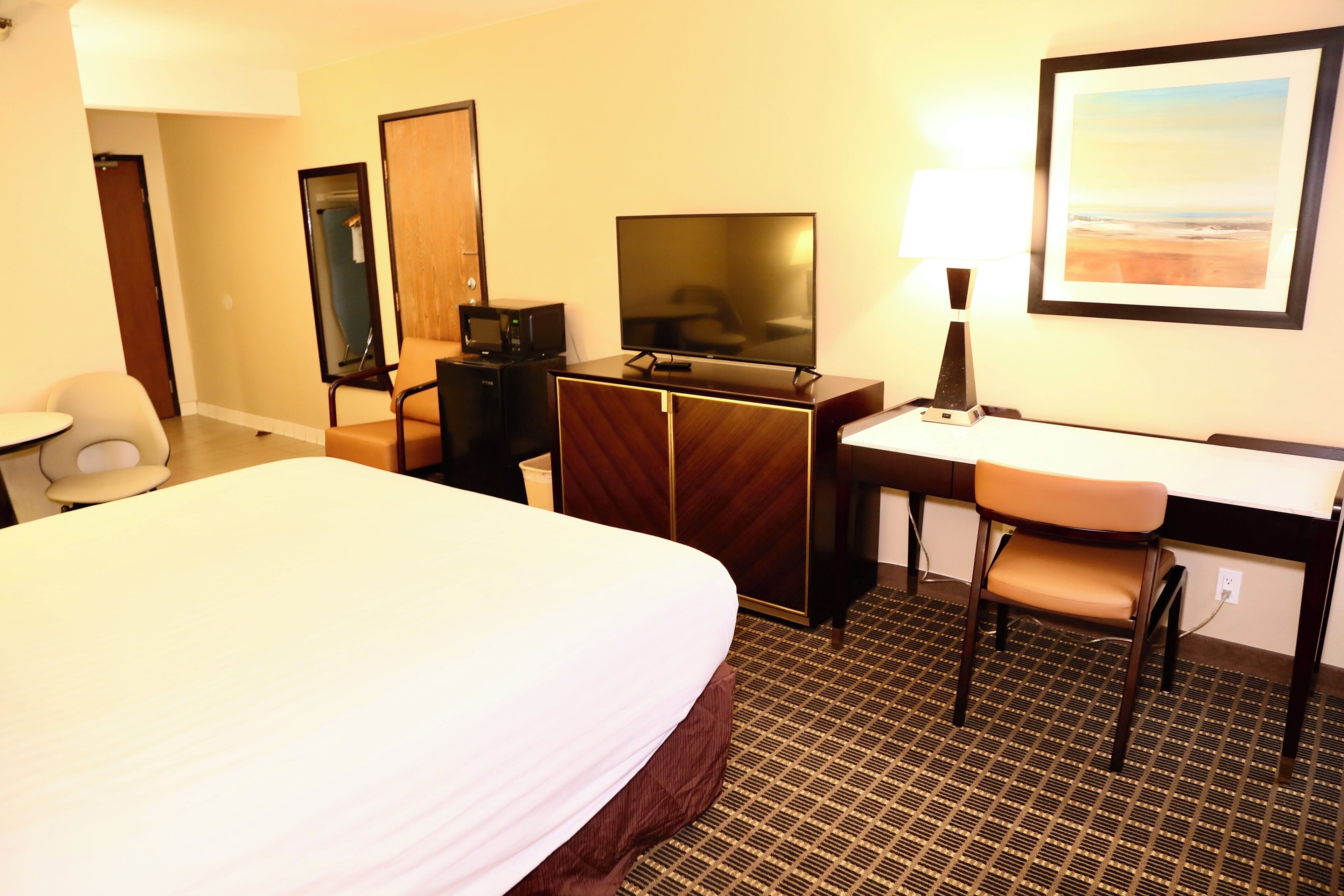 Een hotelkamer met een groot bed, een bureau met stoel, een televisie, een spiegel en een schilderij aan de muur.