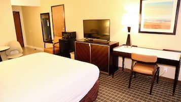 Een hotelkamer met een groot bed, een bureau met stoel, een televisie, een spiegel en een schilderij aan de muur.