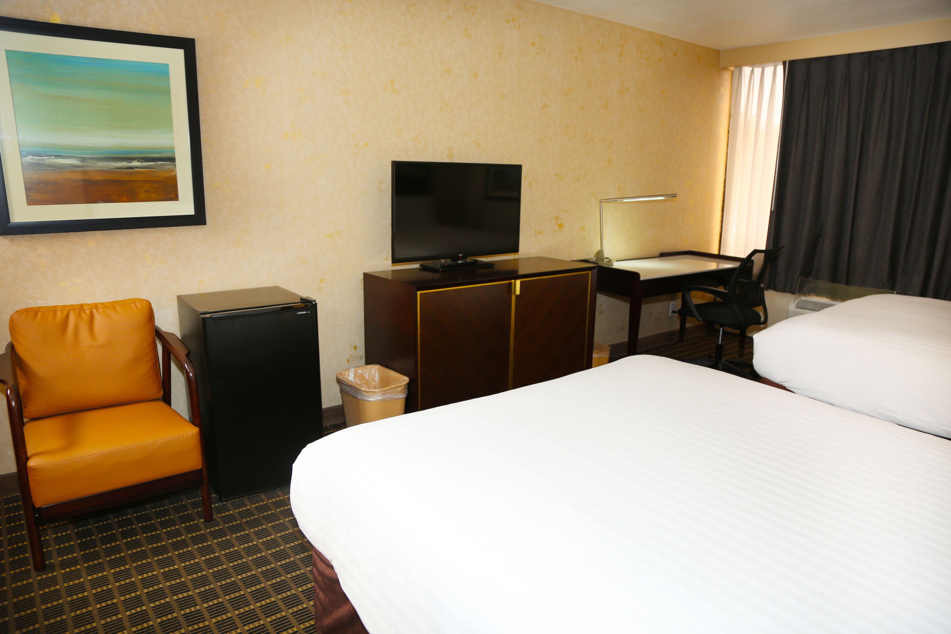 A hotel room with a bed, a desk with a chair, a television, and a trash bin.