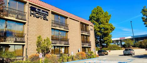A hotel with a brick facade, multiple balconies, and a parking lot with blue handicapped parking spaces.