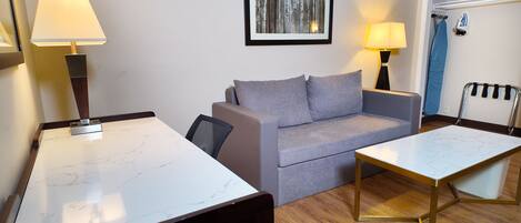 Una habitación de hotel moderna con un escritorio de encimera de mármol, un sofá gris, dos lámparas de pared y un cuadro en la pared.