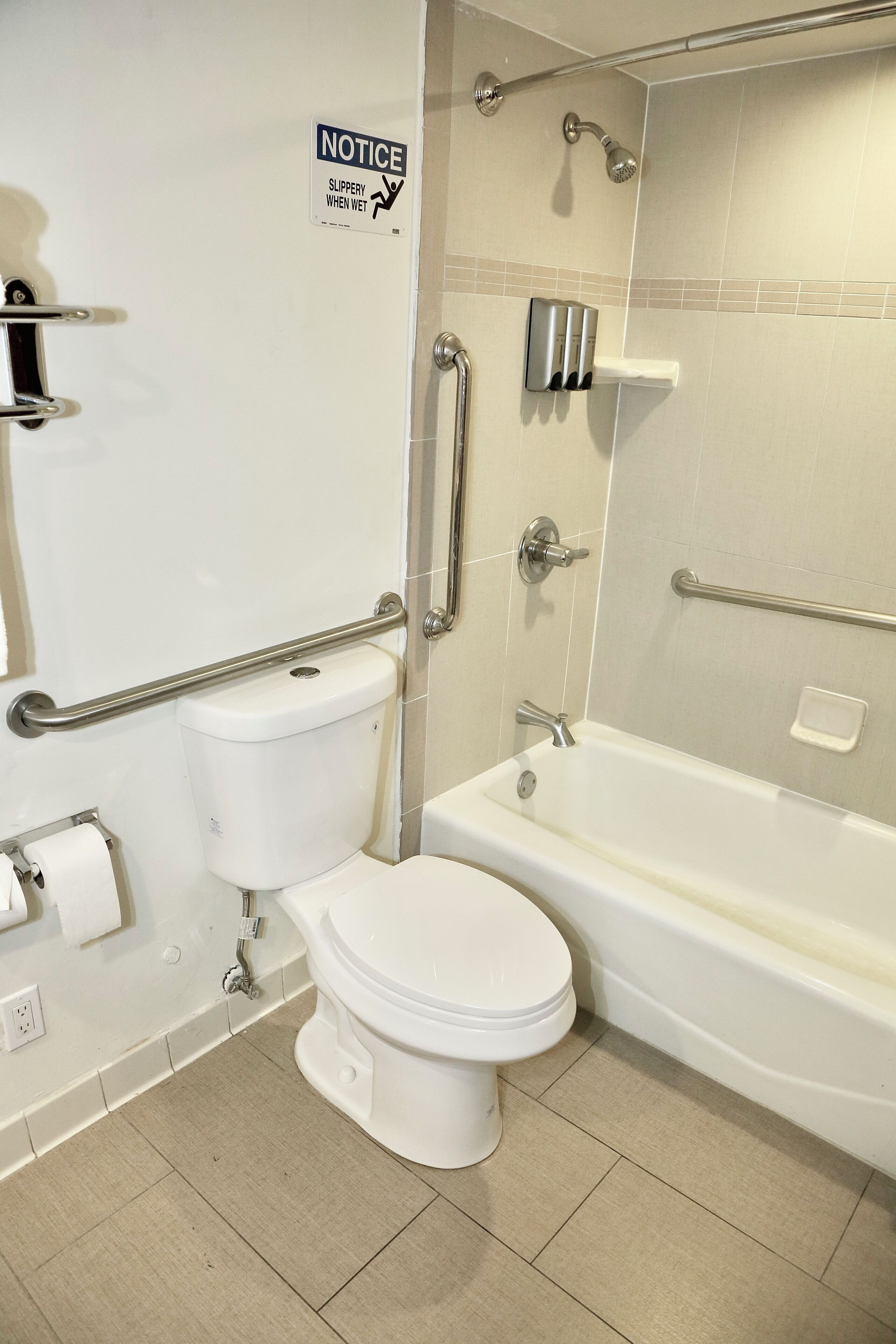 A bathroom with a toilet, a shower with a handrail, and a notice sign.