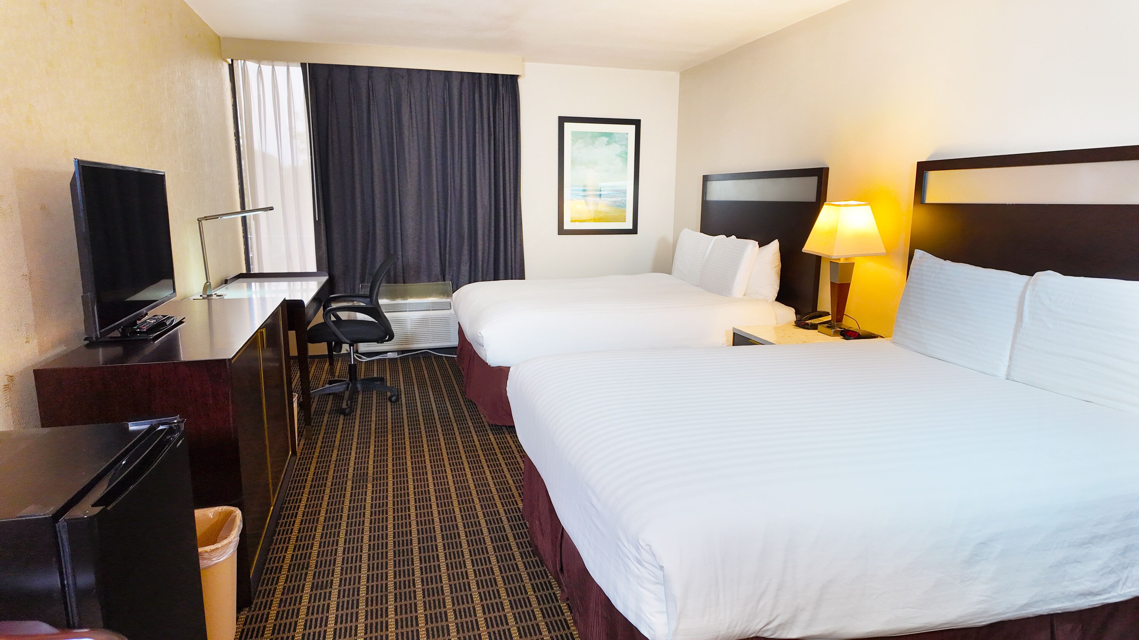 A hotel room with two beds, a desk with a TV, a chair, a lamp, and a picture on the wall.