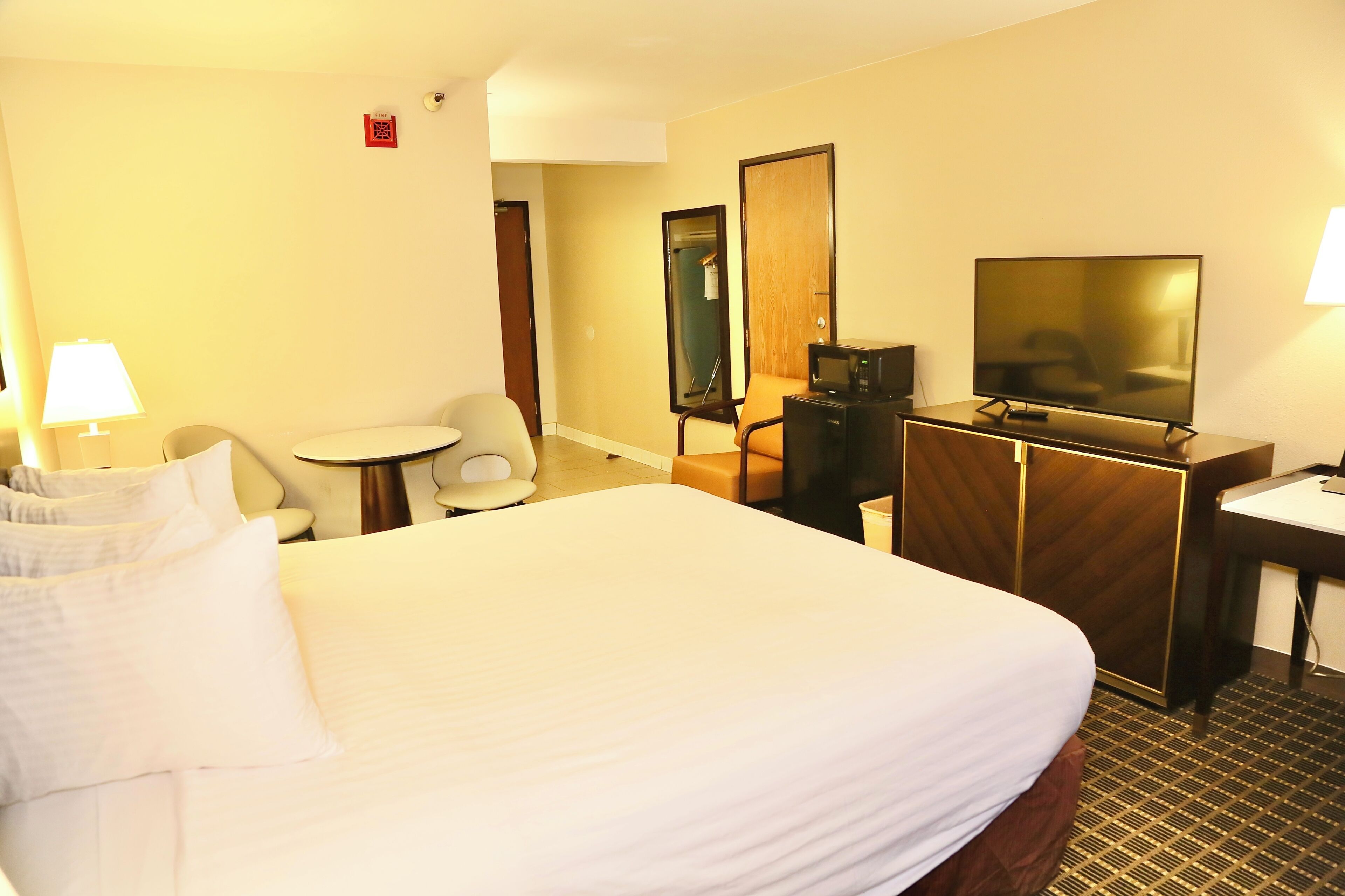 Una habitación de hotel con una cama grande, un escritorio con televisor, una silla y una mesita.