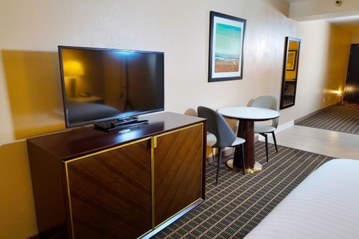 A hotel room with a bed, a TV on a wooden cabinet, a small round table with two chairs, and a framed picture on the wall.