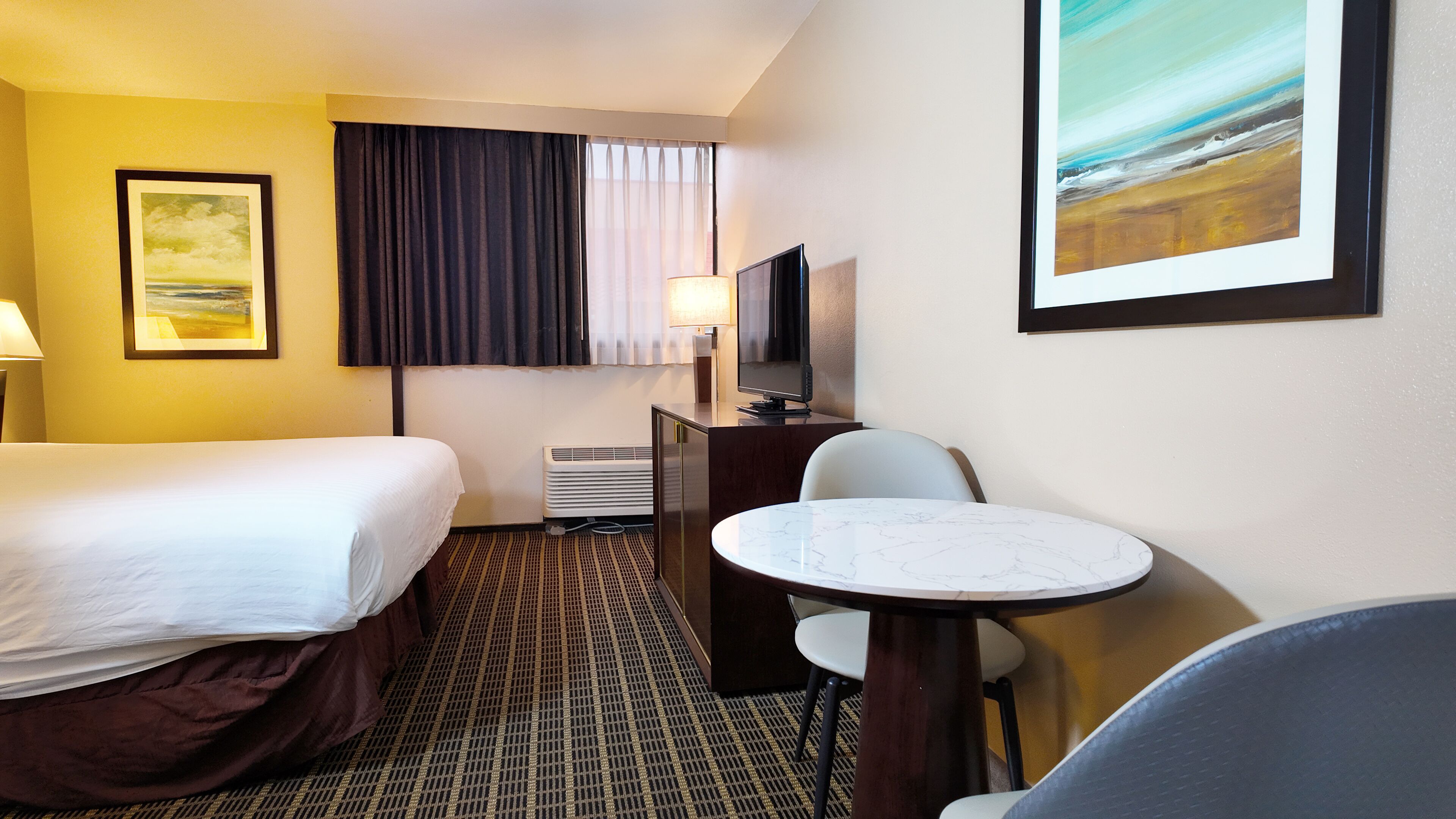 Een hotelkamer met een bed, een bureau, een stoel, een televisie en een schilderij aan de muur.