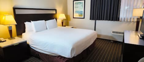 A hotel room with a large bed, two bedside tables with lamps, a headboard, a framed picture on the wall, a window with curtains, and an air conditioning unit.