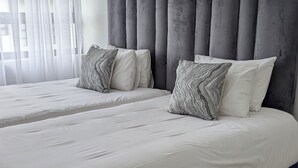 A double bed with a grey upholstered headboard, white bedding, and patterned pillows.