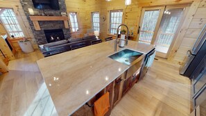 A spacious kitchen with a large island, stone fireplace, and wooden walls.
