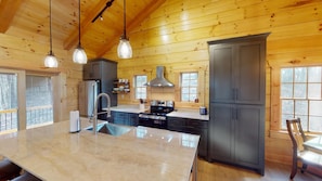 A modern kitchen with wooden walls, a large island, stainless steel appliances, and pendant lighting. - Sunset Ridge Cabin in Hocking Hills (Logan)