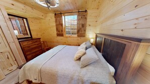 Un dormitorio de cabaña de madera con cama, cómoda y ventana con contraventanas.