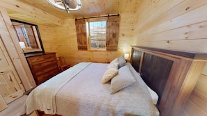 A wooden cabin bedroom with a bed, dresser, and a window with shutters.