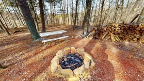 A campsite with a fire pit, a picnic table, and a stack of firewood.