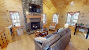 A cozy log cabin interior with a stone fireplace, a comfortable sofa, and a television mounted above it. - Sunset Ridge Cabin in Hocking Hills (Logan)