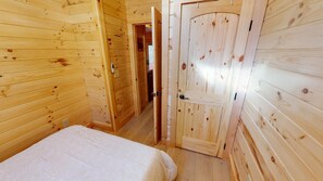 A wooden room with a bed, a door, and a hallway. - Sunset Ridge Cabin in Hocking Hills (Logan)