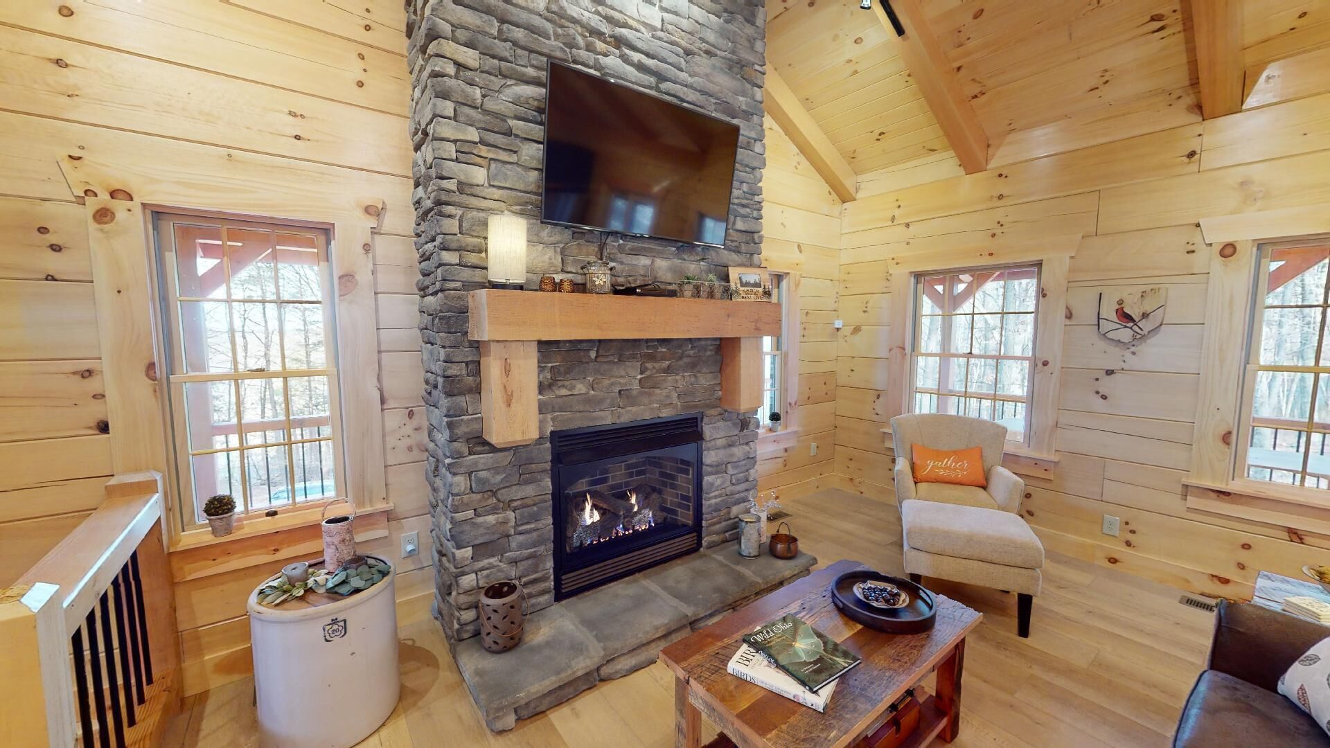 A cozy cabin interior with a stone fireplace, wooden walls, and a comfortable seating area.