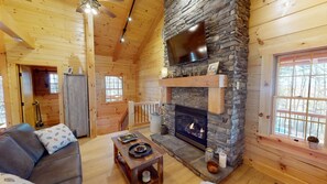 A cozy cabin interior with a stone fireplace, wooden walls, a sofa, and a dining table.