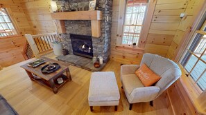 A cozy cabin interior with a stone fireplace, wooden furniture, and large windows.