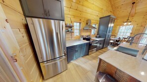 A modern kitchen with stainless steel appliances, wooden walls, and a large window providing natural light. - Sunset Ridge Cabin in Hocking Hills (Logan)