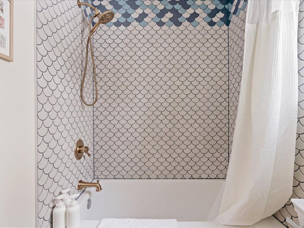 A bathroom with a tiled wall featuring a scale pattern, a shower with a handheld showerhead, and a white towel hanging on the wall.