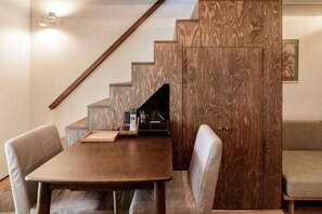 A dining area with a wooden table and chairs, a staircase with wooden steps, and a sofa in the background. - Aoshida Machiya House (Kyoto)