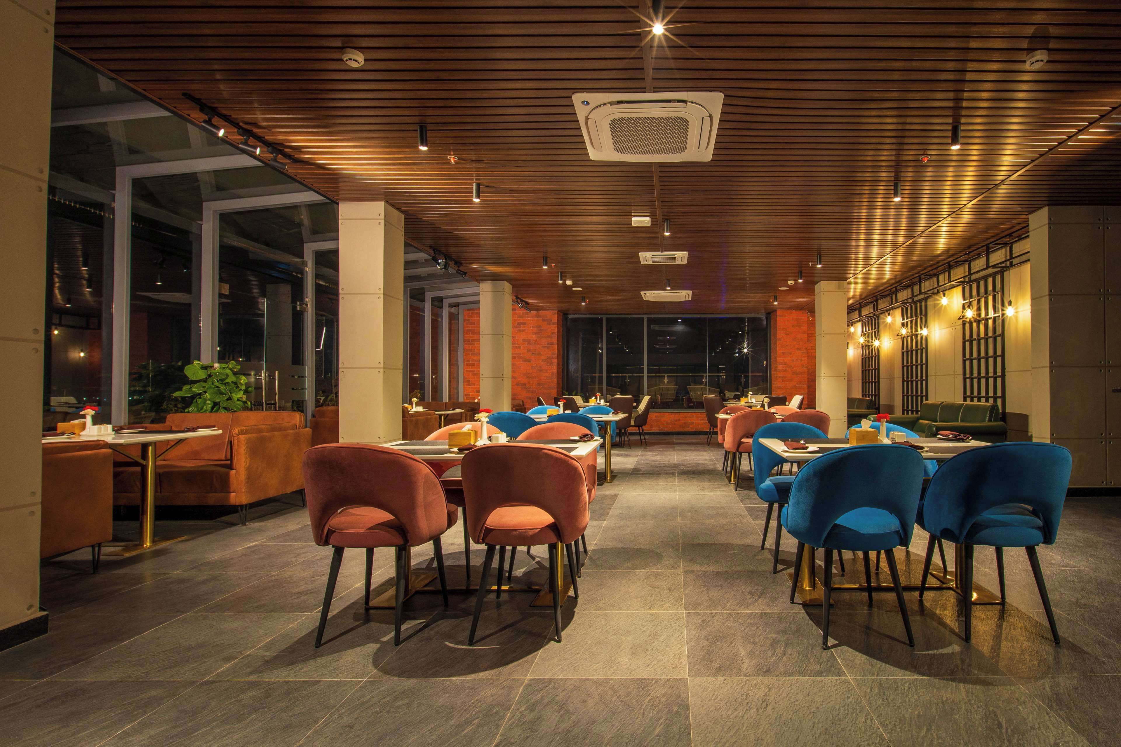 A spacious restaurant with high ceilings, modern lighting, and a mix of seating arrangements including tables and chairs.
