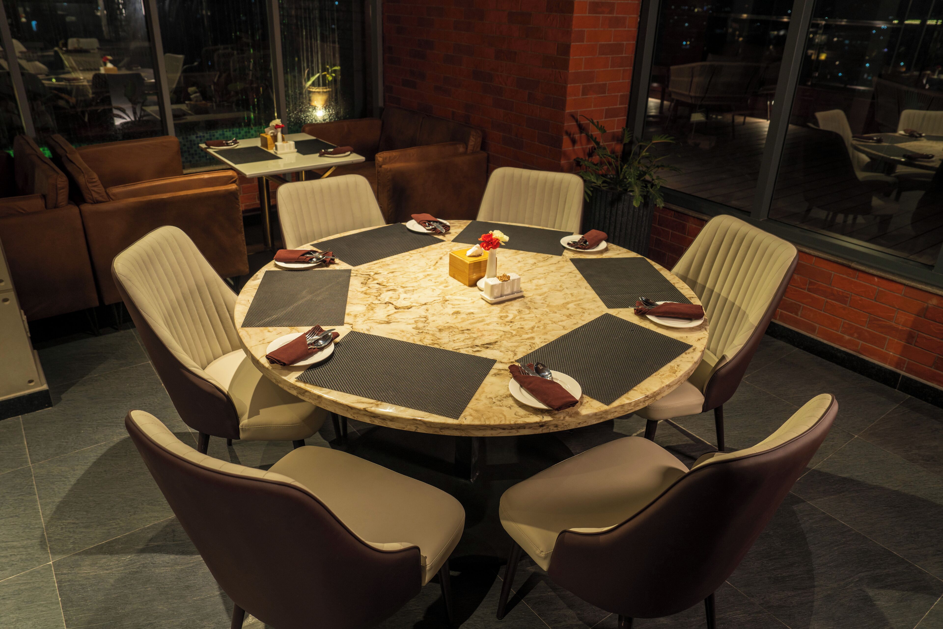 Een ronde tafel met zes stoelen, een vaas met bloemen en borden met bestek.