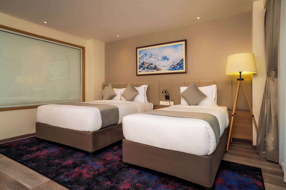 A hotel room with two beds, a large window, a painting on the wall, and a floor lamp.