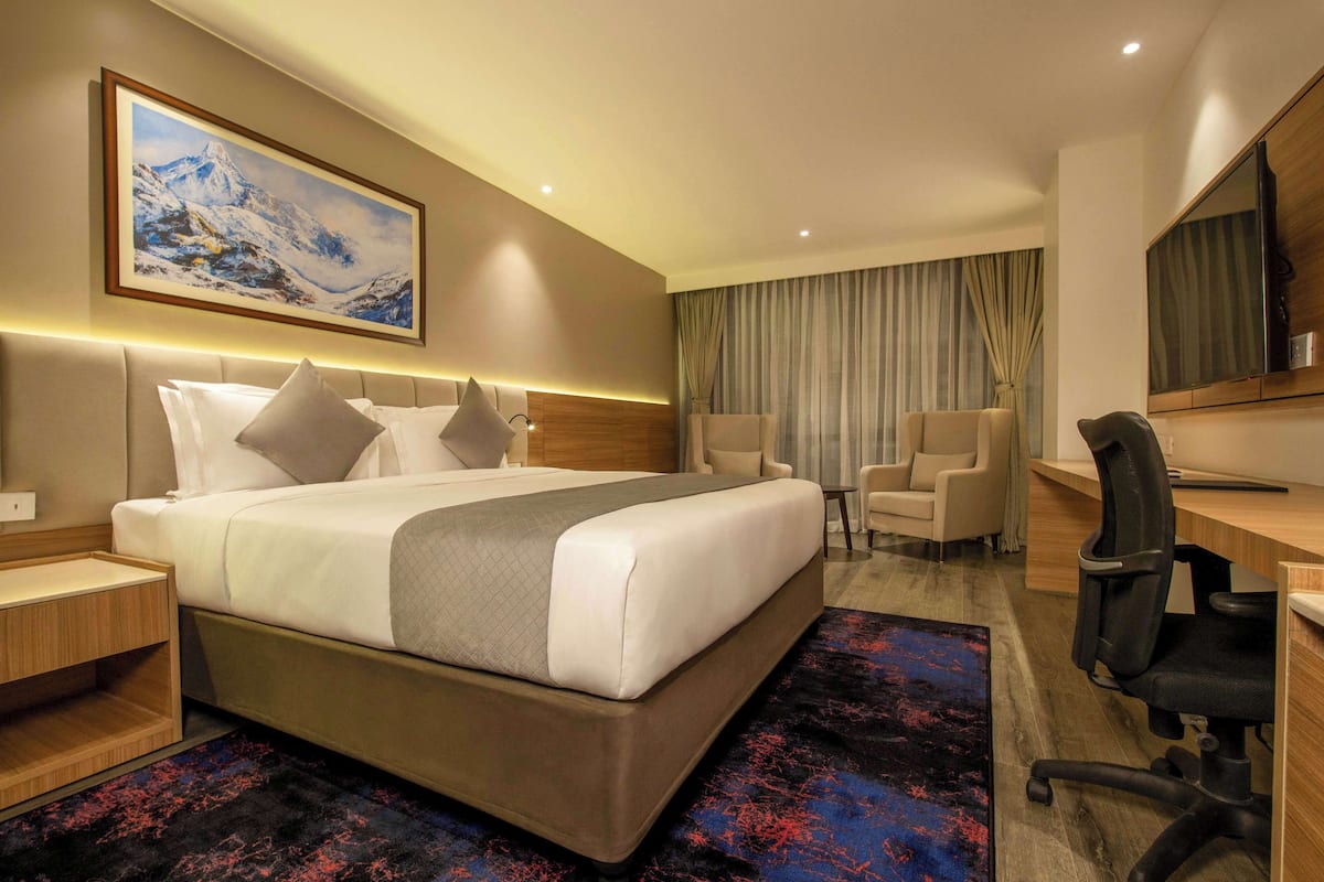 A hotel room with a large bed, a desk, a chair, a TV, and a painting on the wall.