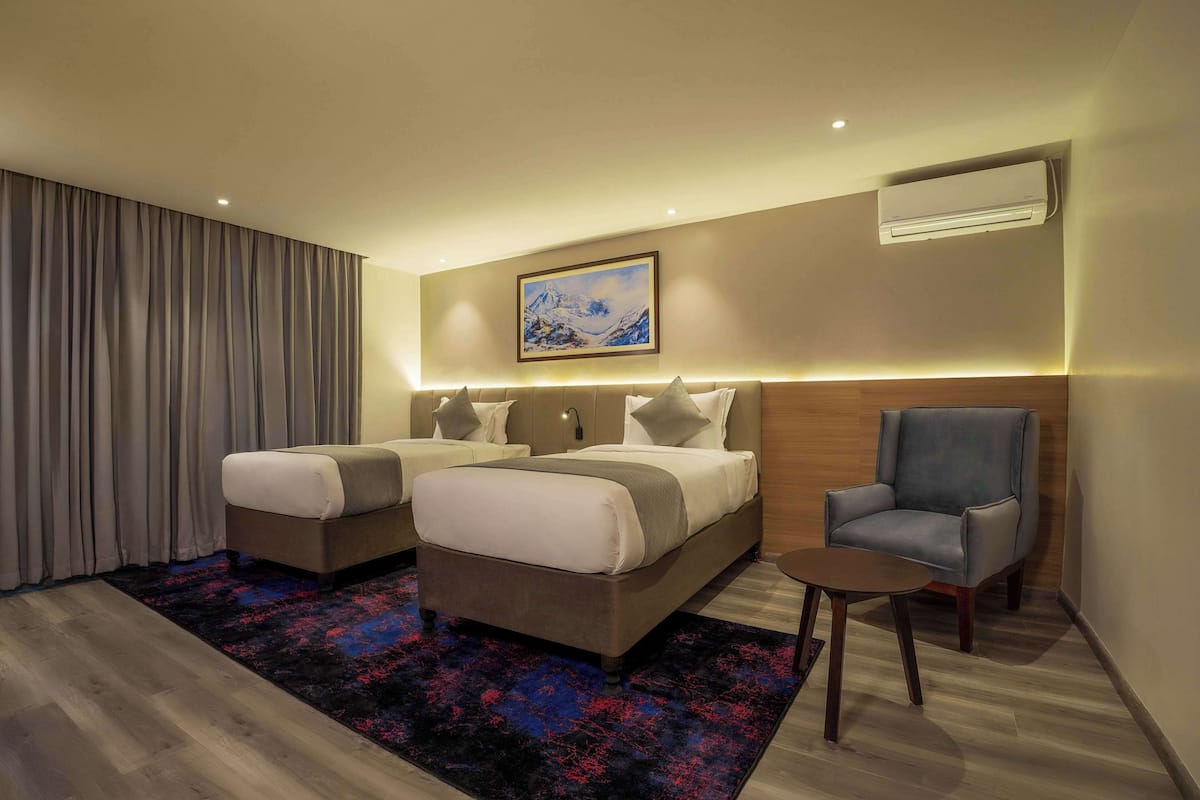 A modern hotel room with two beds, a seating area, and a painting on the wall.
