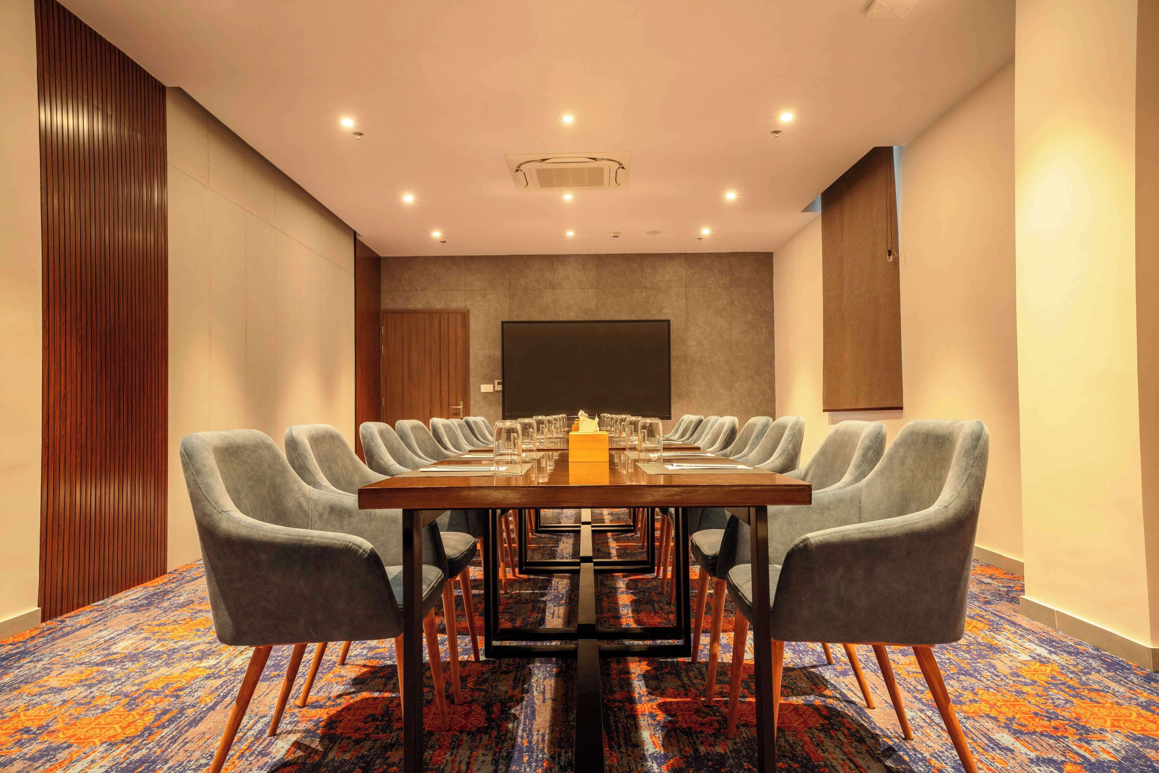 A conference room with a long table, grey chairs, and a patterned carpet.