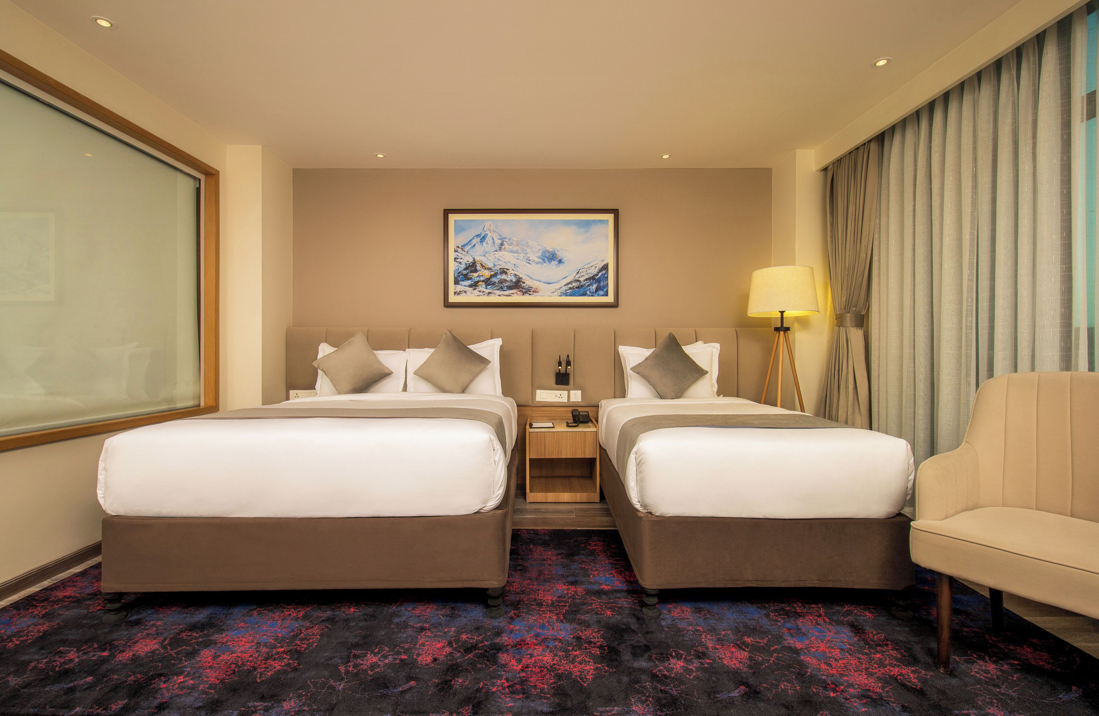 A hotel room with two beds, a nightstand, a lamp, a painting, and a view of the outdoors.