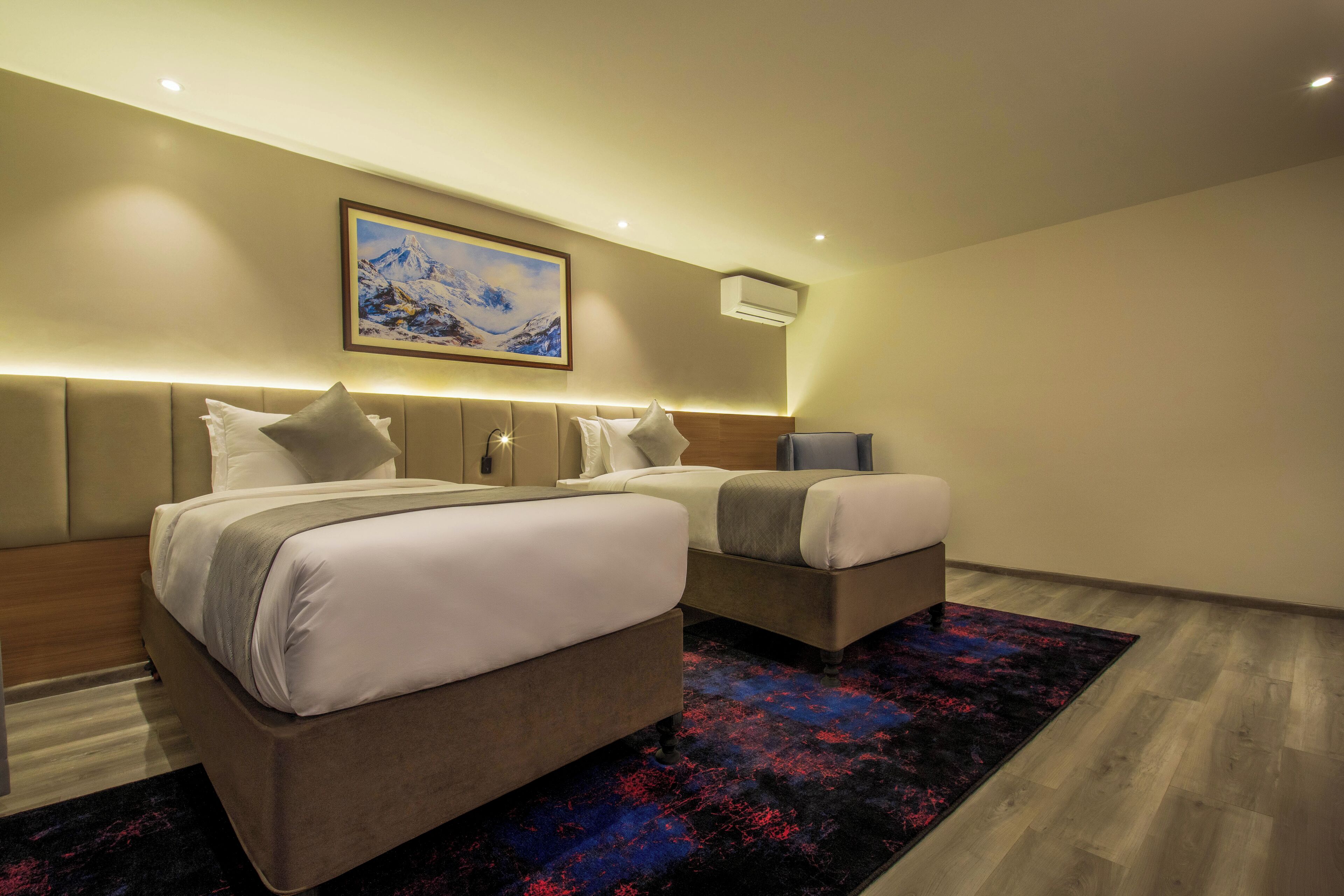 Una habitación de hotel moderna con dos camas, un cuadro grande de una montaña y una alfombra oscura con estampado.