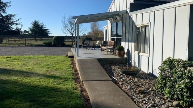 A house with a covered patio area, a lawn, and a gravel path leading to the entrance. - Spires Barn Lodge (Christchurch)