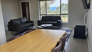 A modern living room with a wooden dining table, two sofas, and a large window offering a view of the outdoors. - Quiet house with great views and a 5 min drive to town (Wallan)