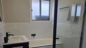 A modern bathroom with a bathtub, a glass-enclosed shower, and a window above the sink. - Quiet house with great views and a 5 min drive to town (Wallan)