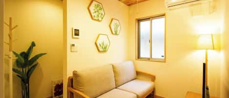 Una habitación con techo de madera, un sofá, una planta en maceta e impresiones botánicas enmarcadas en la pared.